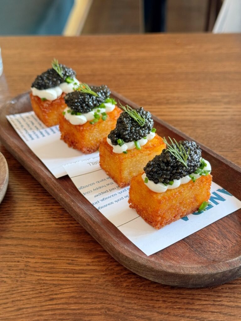 Rectangular bites with caviar on top on a wood plate. 