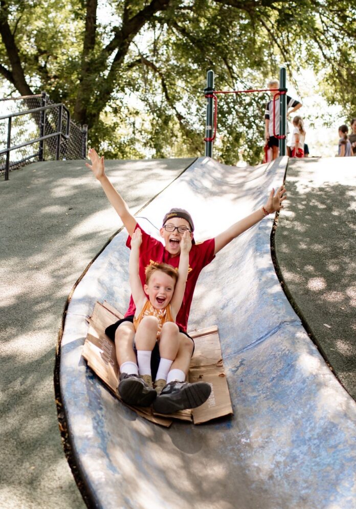 Two kids come down a blue slide in Pittsburgh.