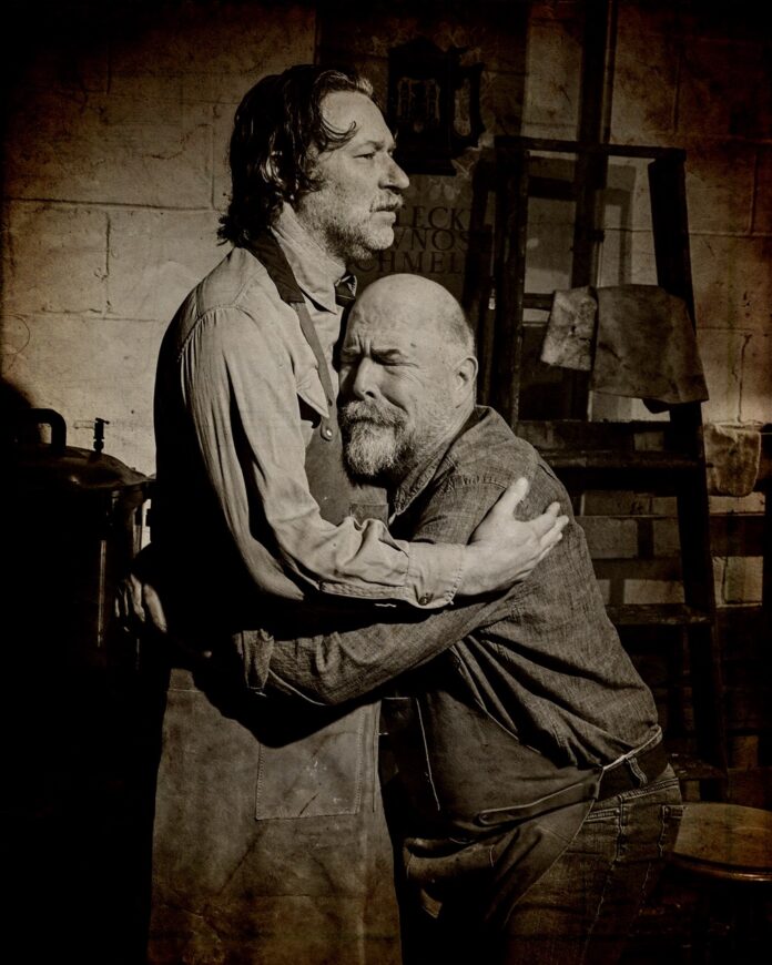 Two men hugging in a black and white theater image.
