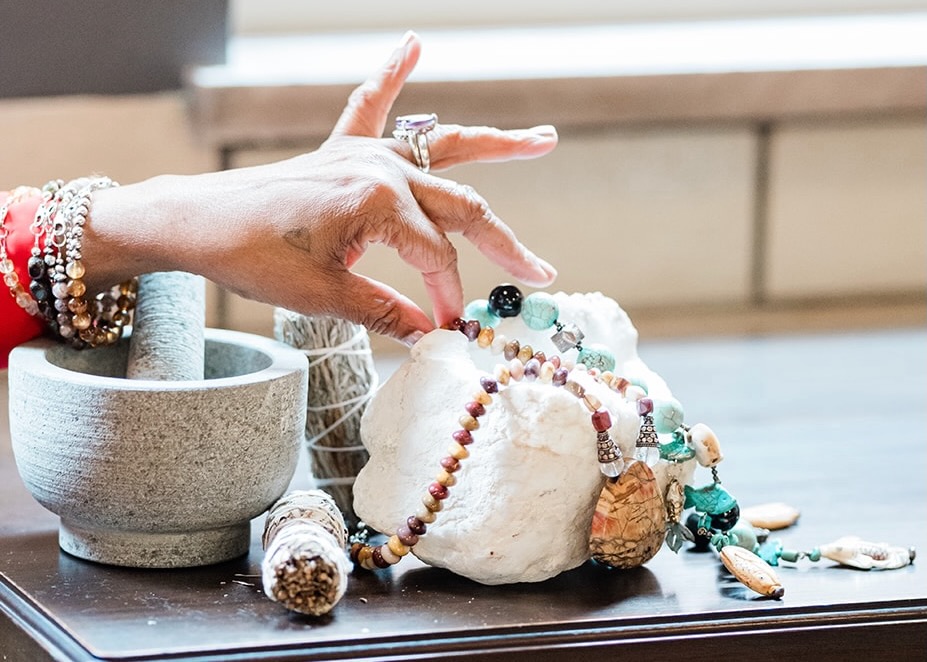 A woman picks a bead necklace off a crystal rock.