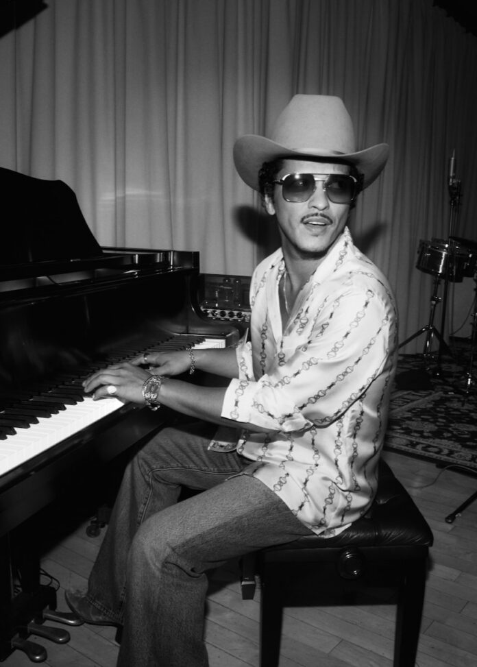 Bruno Mars at a piano with a cowboy hat on.
