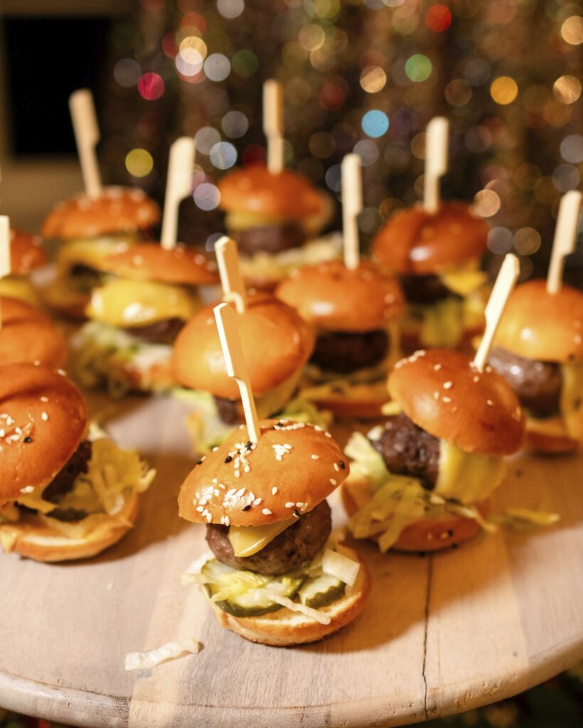 A wooden board with several miniature hamburgers help together with appetizer toothpicks.
