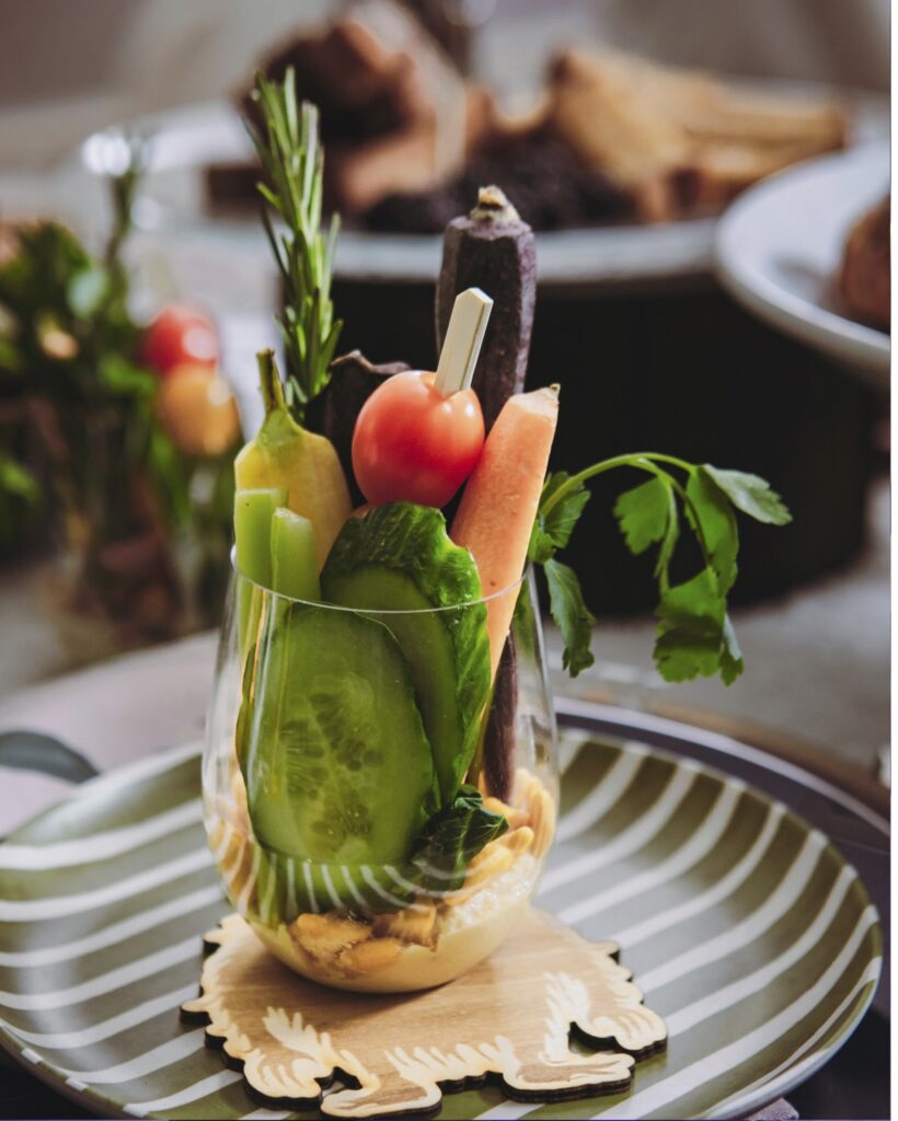 A stemless wine glass on a striped plate filled with fresh vegetables and hummus at the bottom.