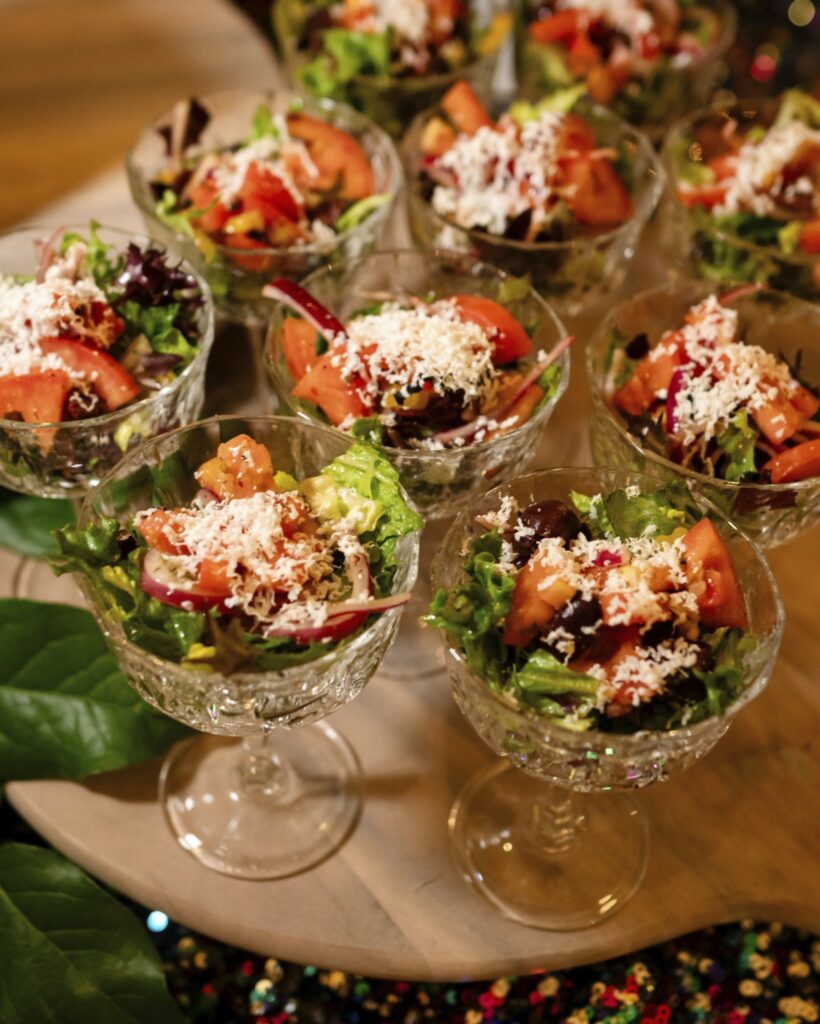 Several stemmed glasses with small salads covered with grated cheese.