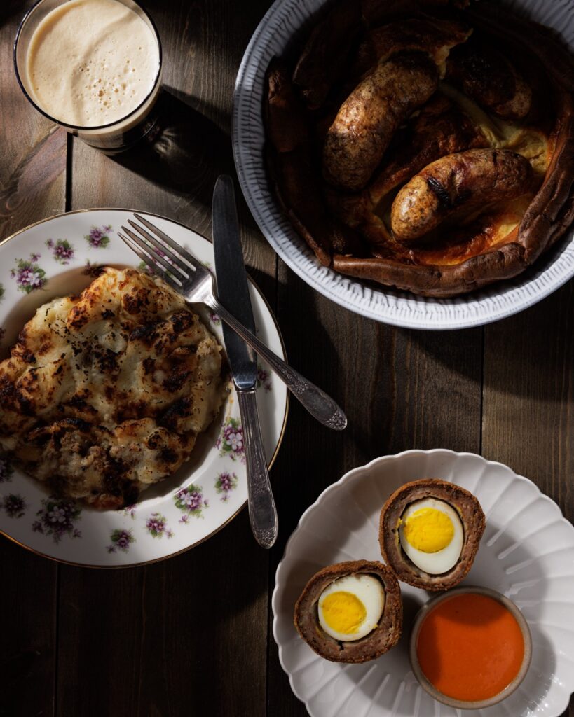 Three white plates with scotch eggs, stew, and a set fork and knife.
