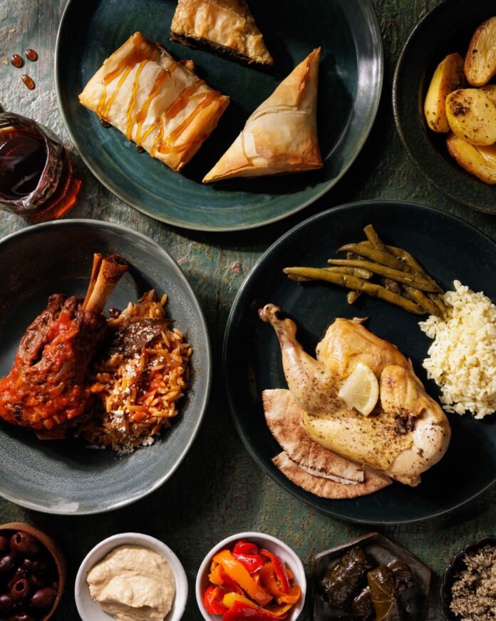 A table full of cultural cuisine dishes on green plates like chicken and rice, greek pastries, and African beef.