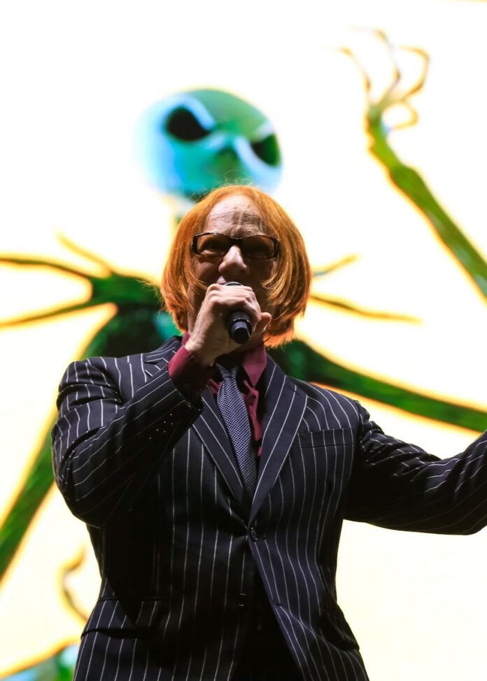 Danny Elfman sings in front of a screen with jack skellington on it at a classical concert.