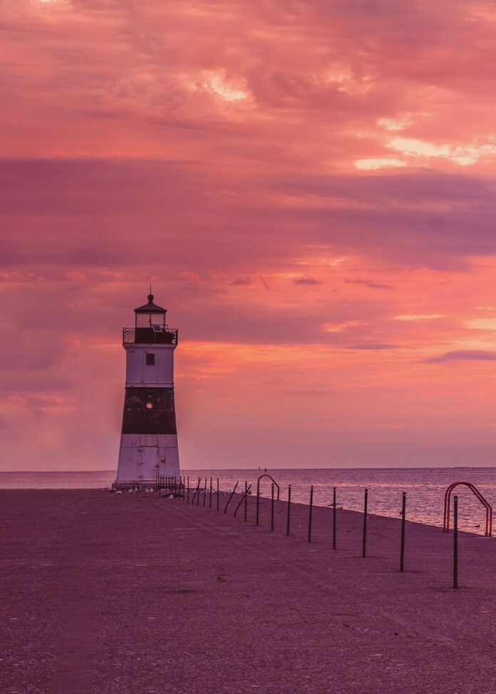 A lighthouse at Presque Isle State Park in a pink sky.