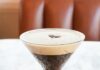 Where to Get the Best Espresso Martini in Pittsburgh An espresso martini on a white marble table with a foam and three coffee beans for garnish.