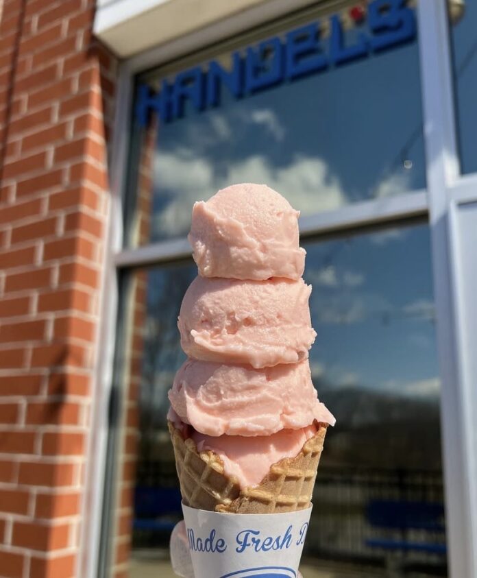 A pink colored ice cream in a sugar cone.