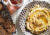 6 Hummus Recipes That Take You Beyond the Basic Chickpea Two bowls of hummus, one lemon artichoke and the other triple tomato sit on a white picnic table with wheat crisps nearby.