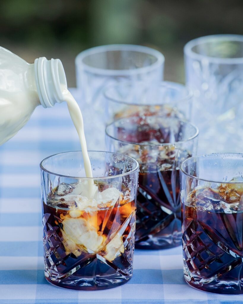 A person pours milk into a glass of coffee.