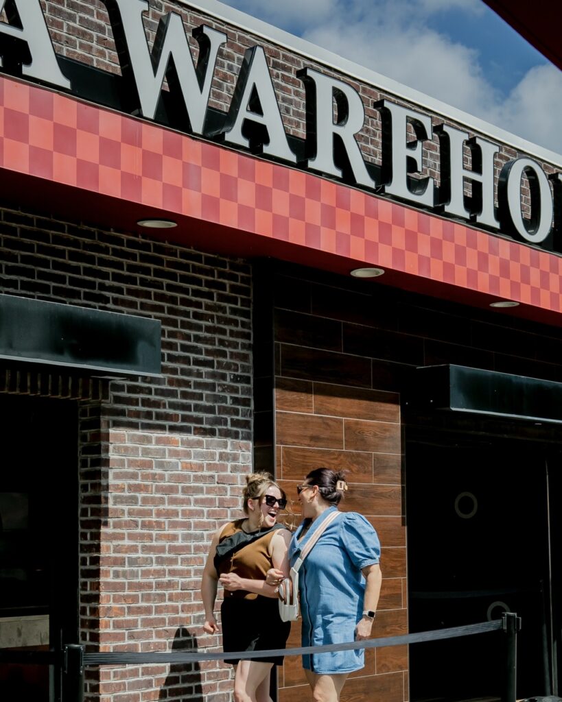 Two women walk by pizza warehouse.