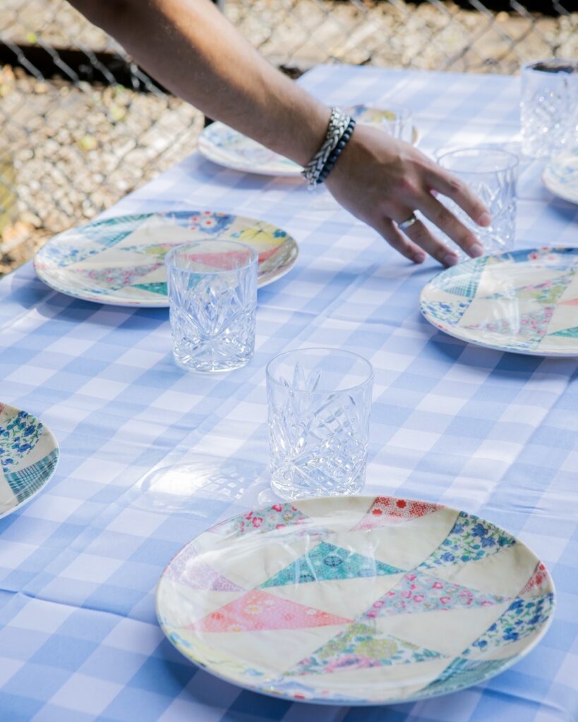 A woman sets down drinking glasses with pattern plates on a tablecloth.