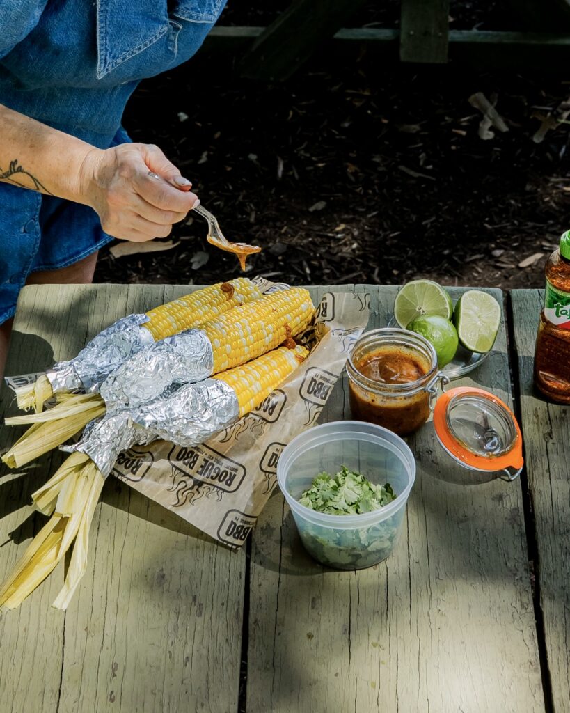 A person dresses corn with a sauce.