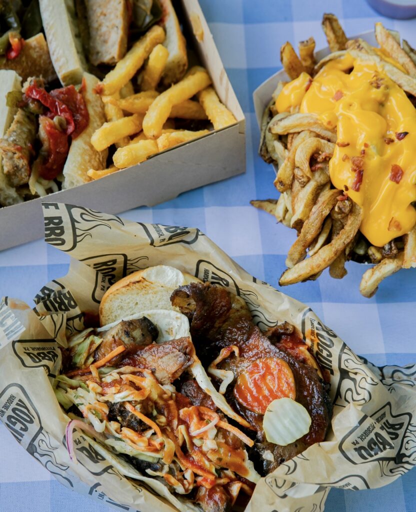 Three carriers of food like fries, sausage, and BBQ.