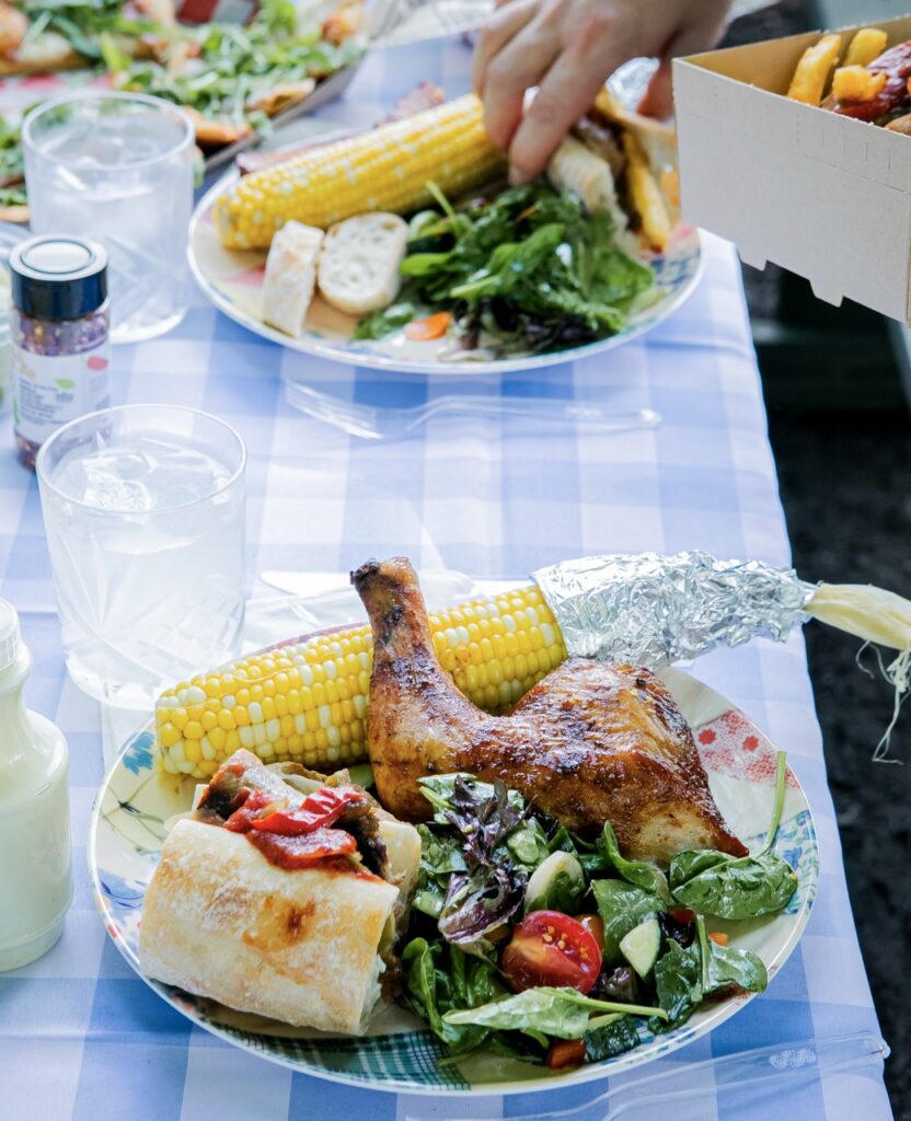 A plate full of salad, sausage, chicken, and corn.
