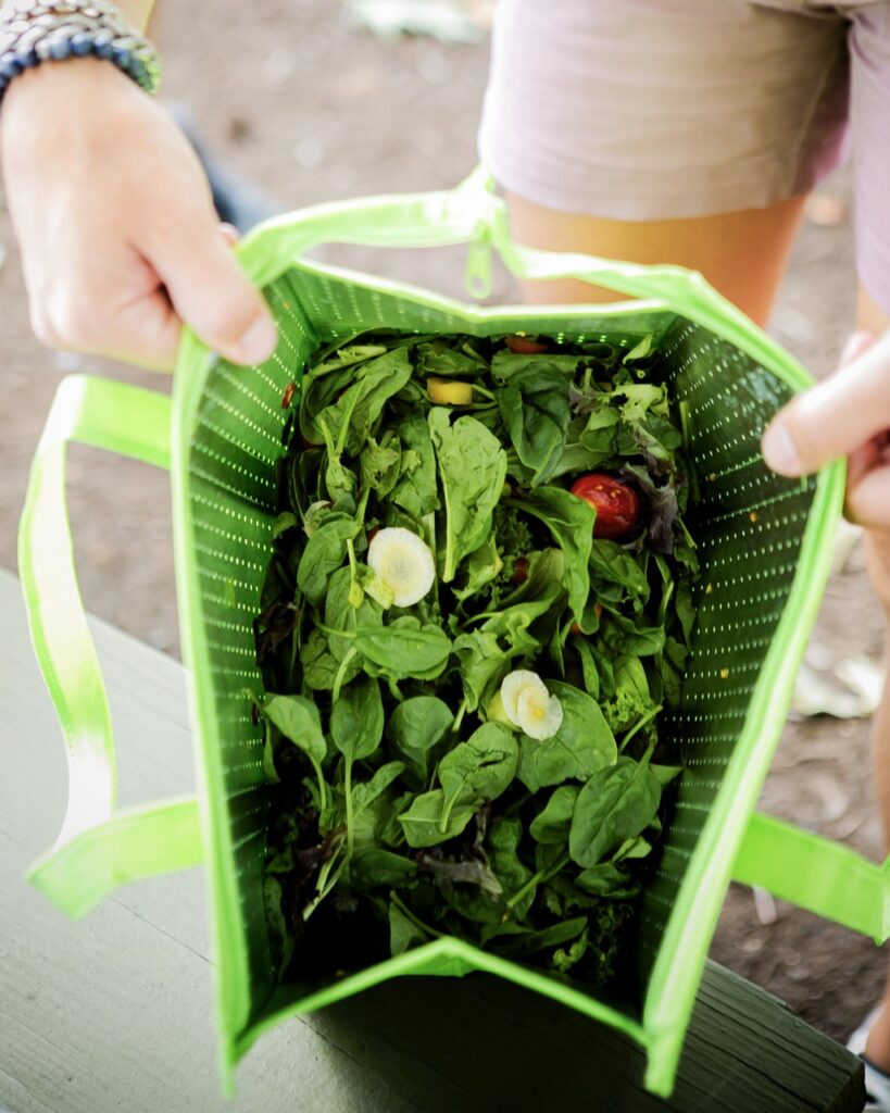 A person opens a tote bag full of salad.