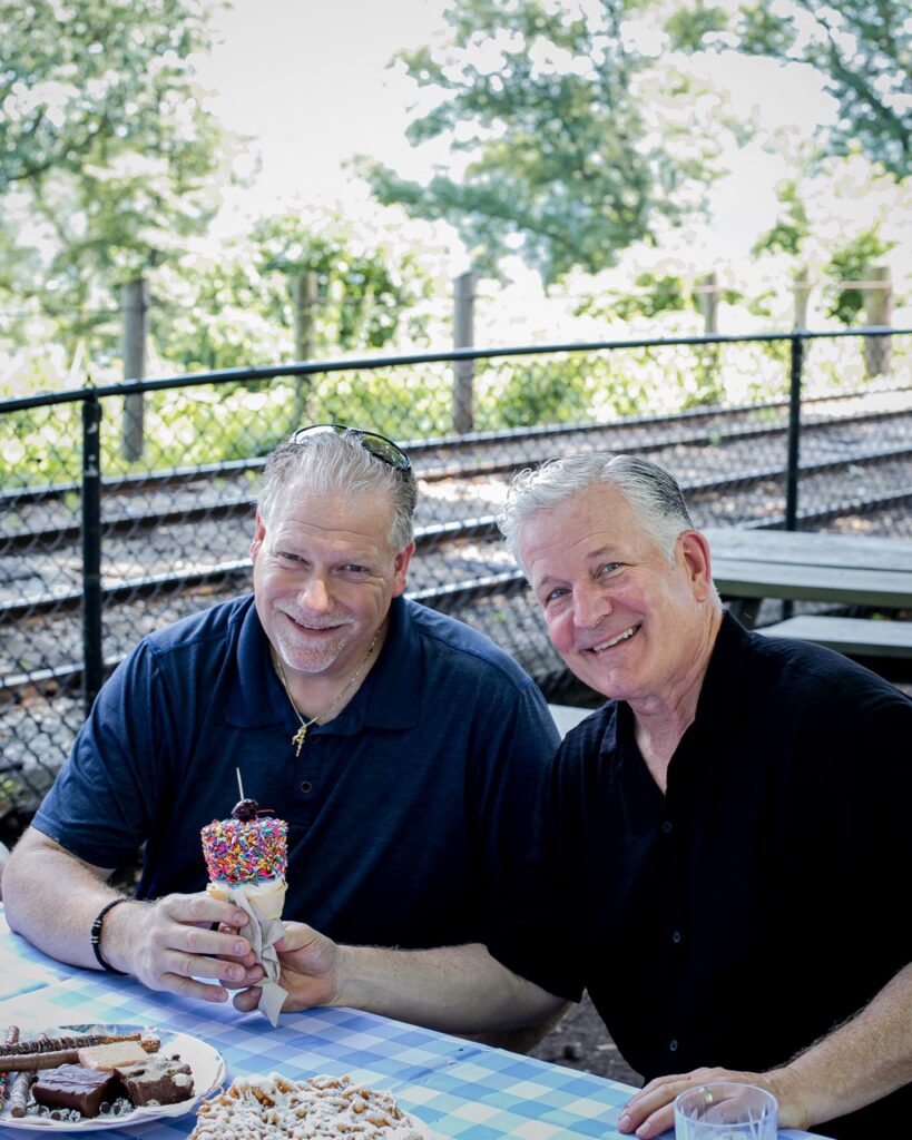 Two men hold an ice cream cone.