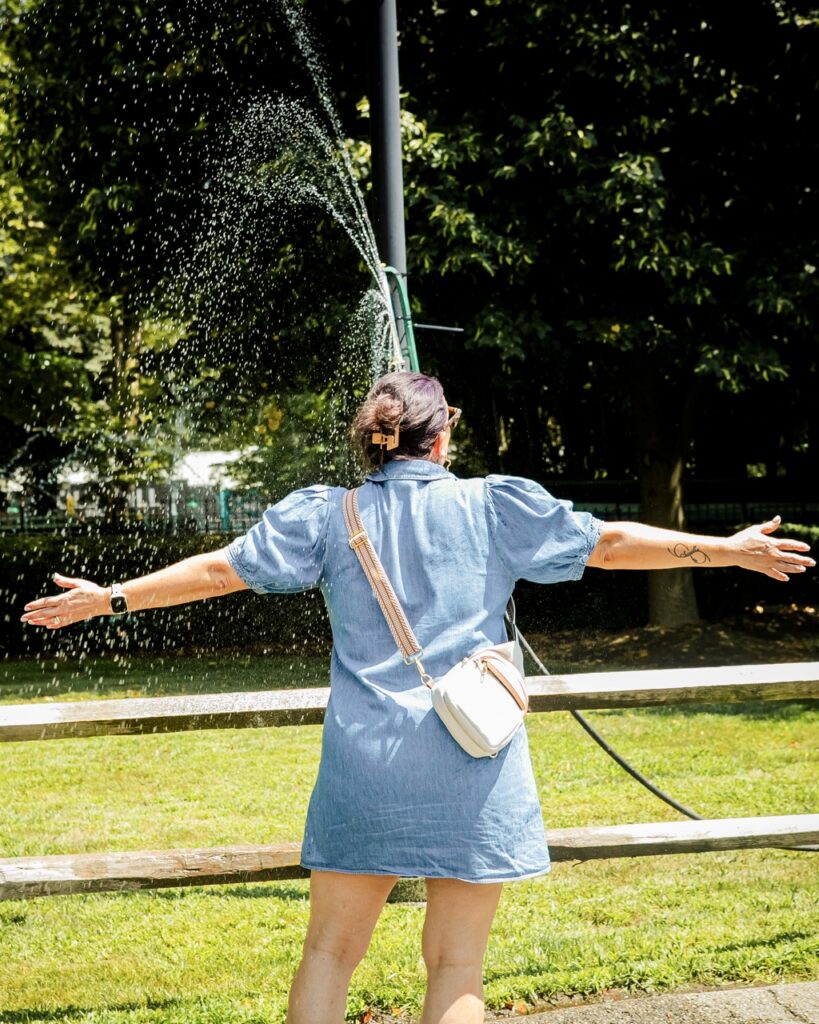 A woman stands in a sprinkler.