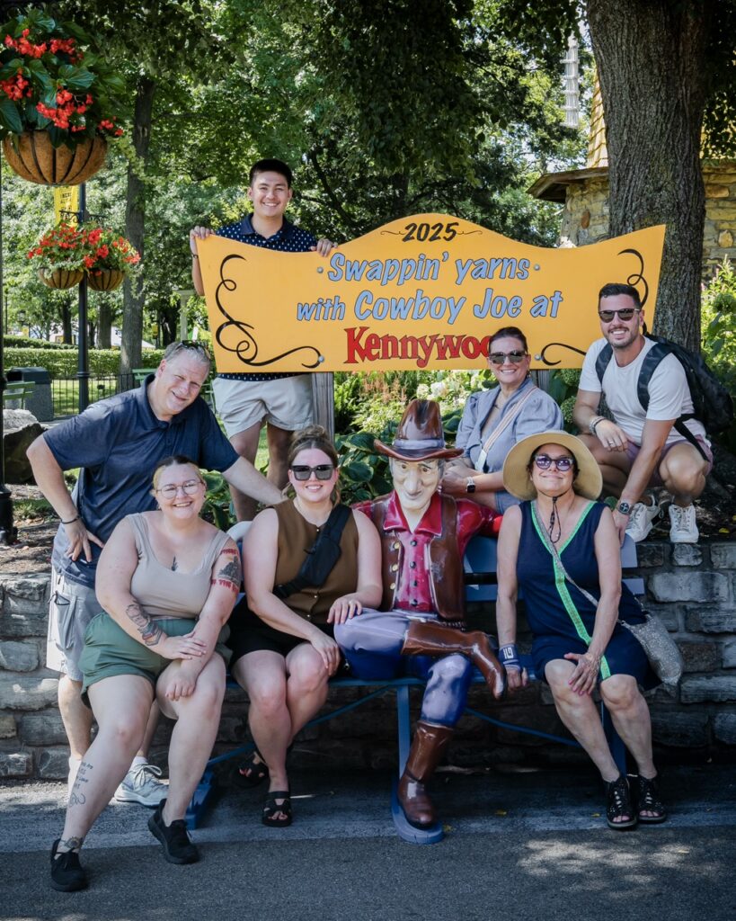 A group of TABLE workers sit on a bench by a cowboy statue.