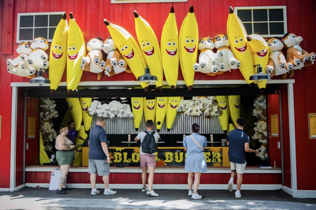 Five people line up at a red game booth with large prizes.