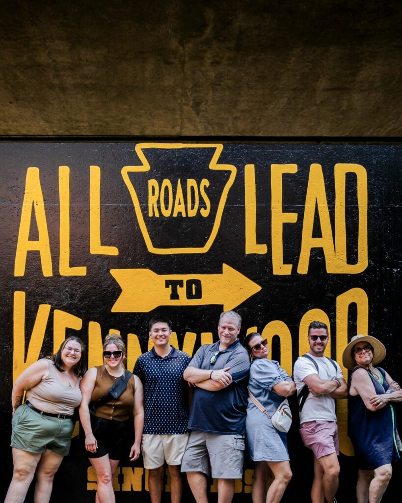 A group of TABLE Magazine workers in front of a black Kennywood sign.
