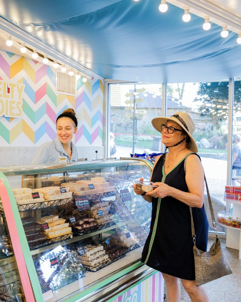 A woman in a hat holds sweets from a girl at the fudge counter.