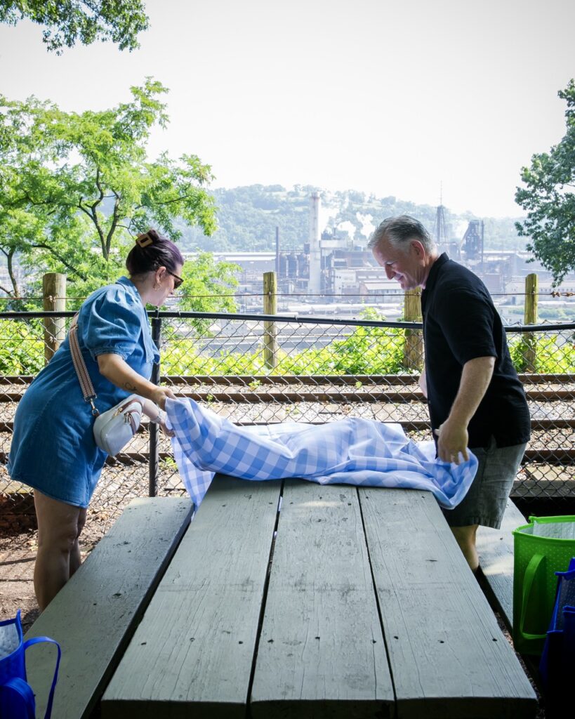 A man and woman arrange a cloth on a picnic table.