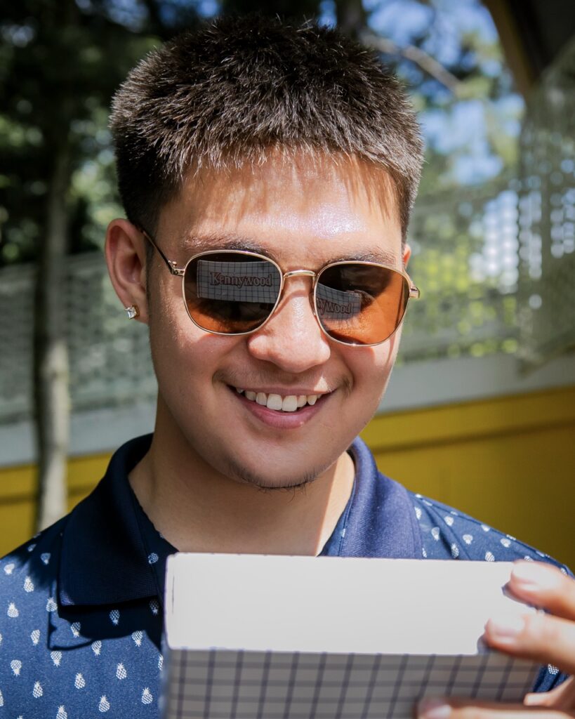 A man looks at a Kennywood fudge box in his sunglasses reflection.
