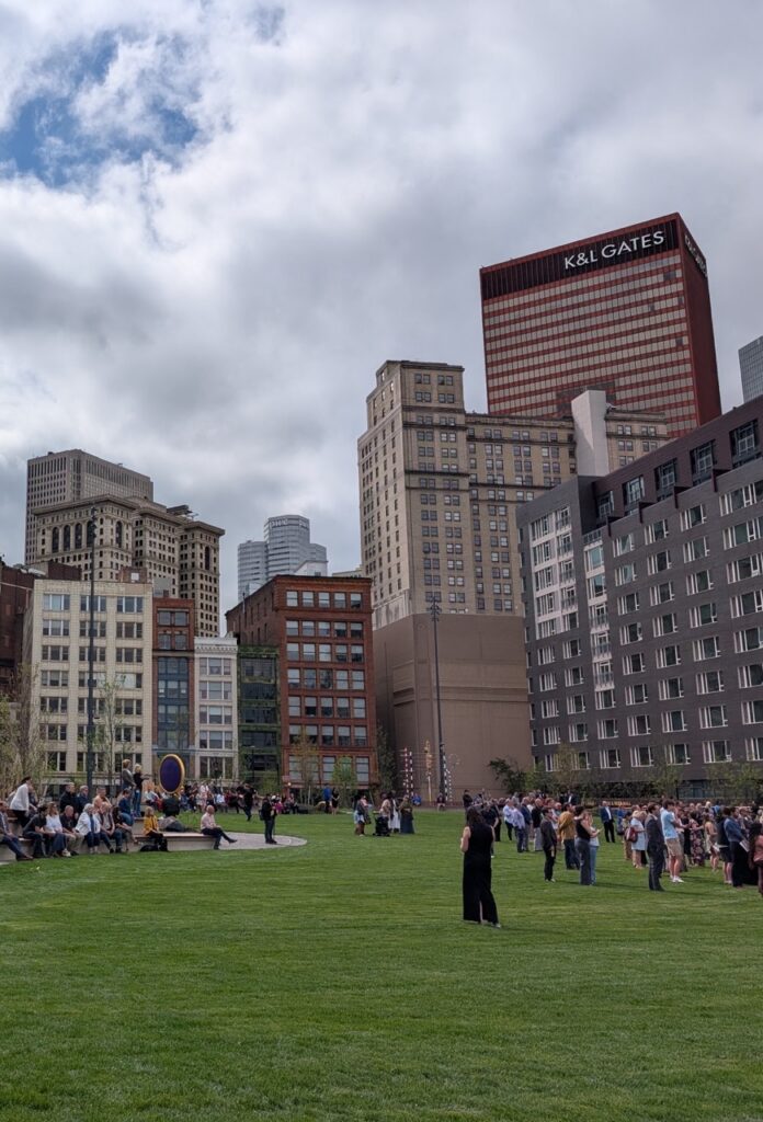 Arts Landing in Pittsburgh Downtown with people walking among the grass and tall buildings in the background.