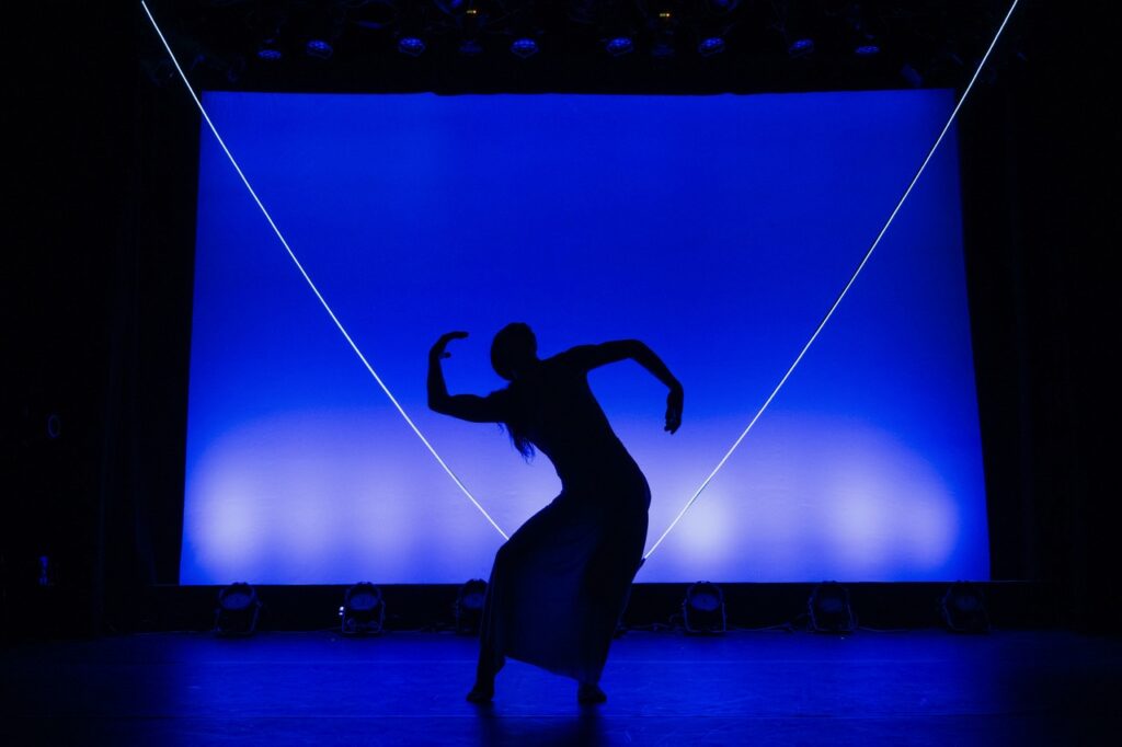 A person dances in front of a bright blue background showing only their shadow.