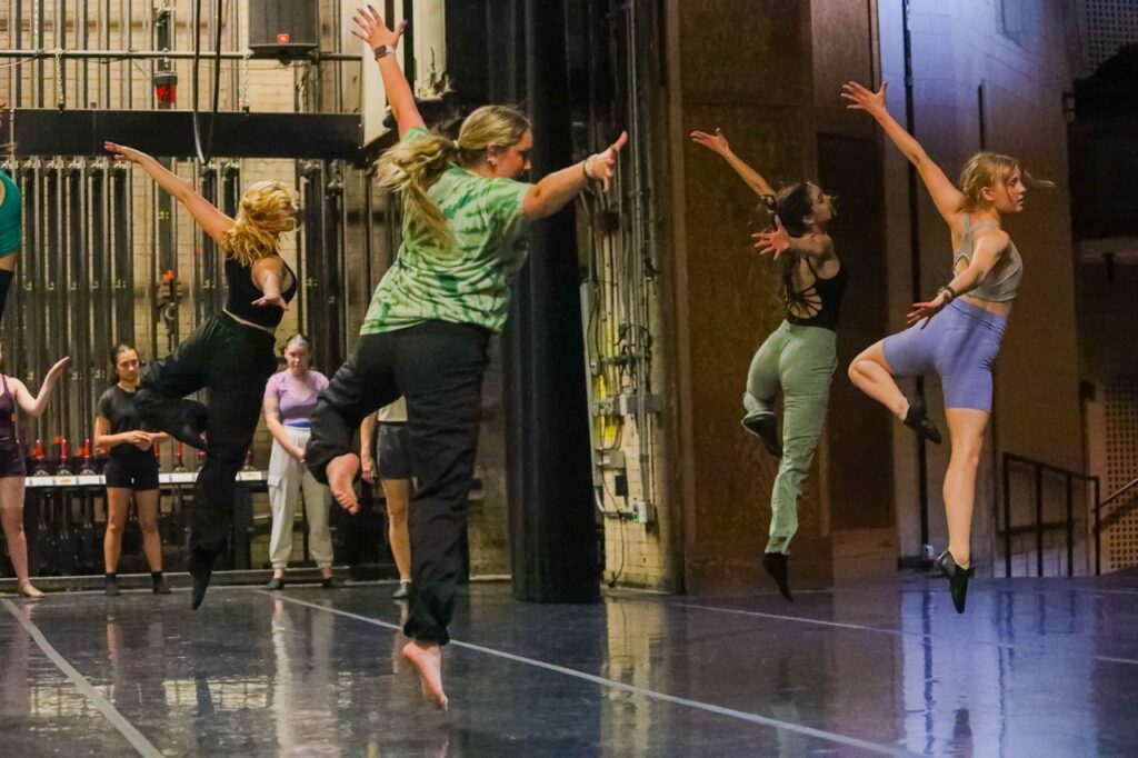 A group of dancers leap with their arms out on stage.