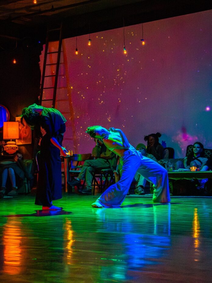 Two people dance on stage in multi-color lights, bending backwards.
