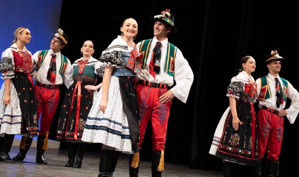 A group of dancers in old school German clothing in dresses, pants, vests, and hats.