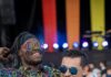 Pittsburgh Pride Month Events for Everyone Two men in rainbow outfits and sunglasses stand in front of pride flag colors on a stage.