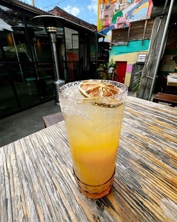 A yellow margarita in a tall glass with a dried lime garnish sits on a dining table.