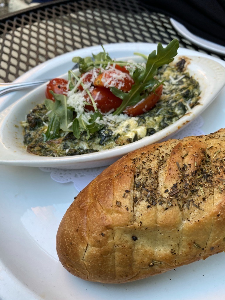 A load of sliced bread beside a bowl of spinach and artichoke dip.