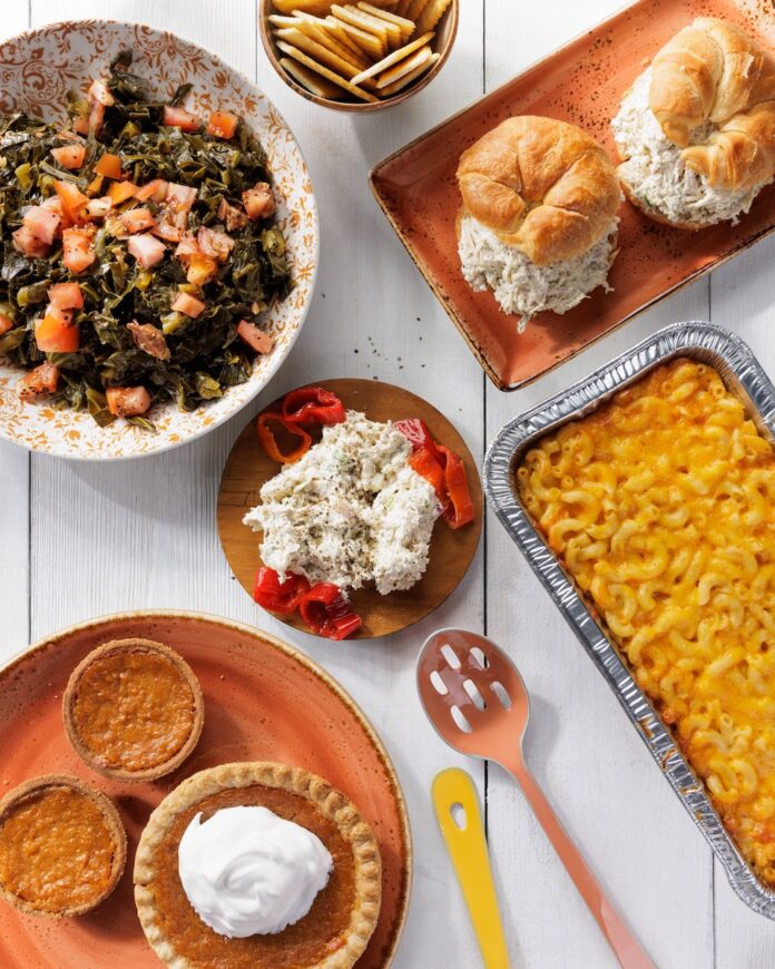 A white picnic table with tuna salad croissants, mac and cheese, sweet potato pie, and greens.