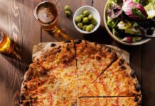 8 More Delicious Pizza Places to Explore in Pittsburgh A large cheese pizza sits on a wood table with big and small bowls of sides and salads.