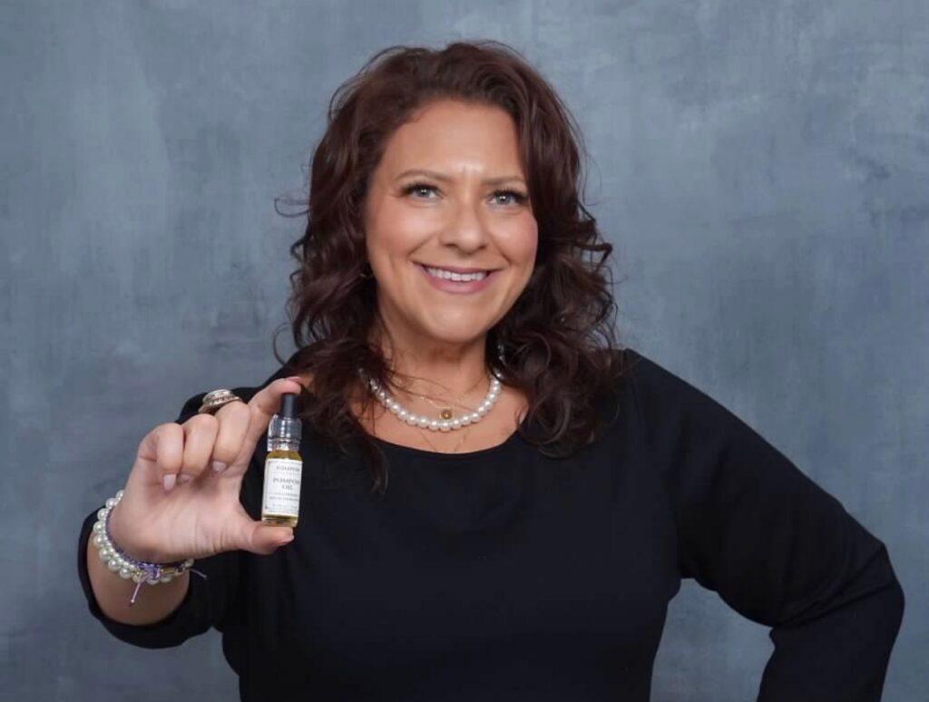 A woman (Kelly Cheatham Lapinsky, founder of Pom Pom Oil - From Earth to Skin) holding a bottle of Pom Pom oil for the camera.