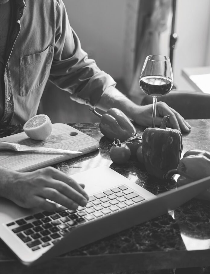 A person at a computer with a glass of wine and peppers.