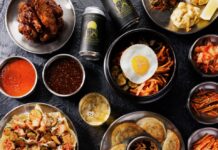 Rick Sebak’s Favorite Places to Eat in Western Pennsylvania A black table full of plates featuring dumplings, Korean beef, stir fry, cans of beer, and little bowls of vegetable sides and sauces.