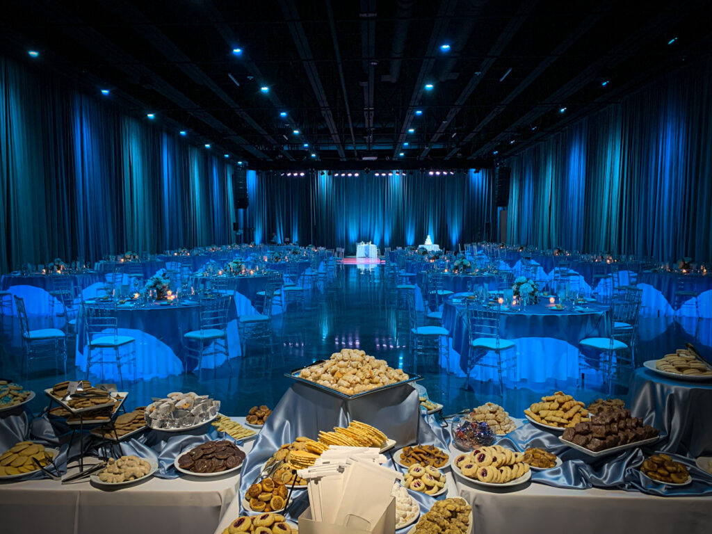 The ballroom at the Rivers Casino decorated for a wedding with a cookie table at the forefront of the photo and the room washed in blue lights.