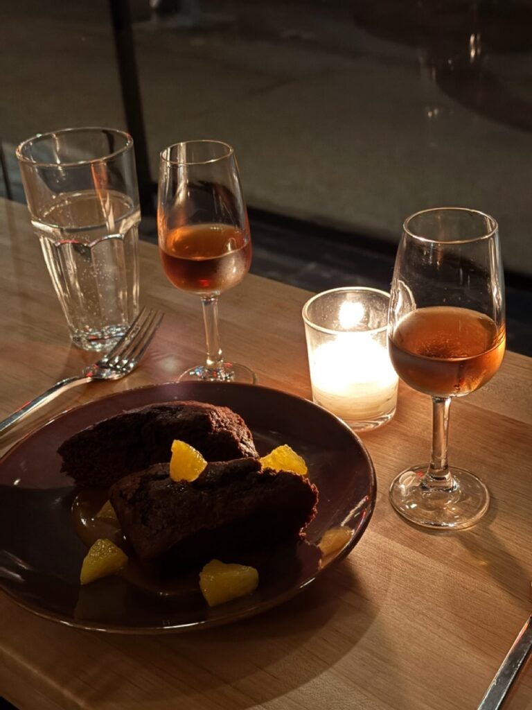 Two wine glasses on a table with a plate in between them and candlelight. 