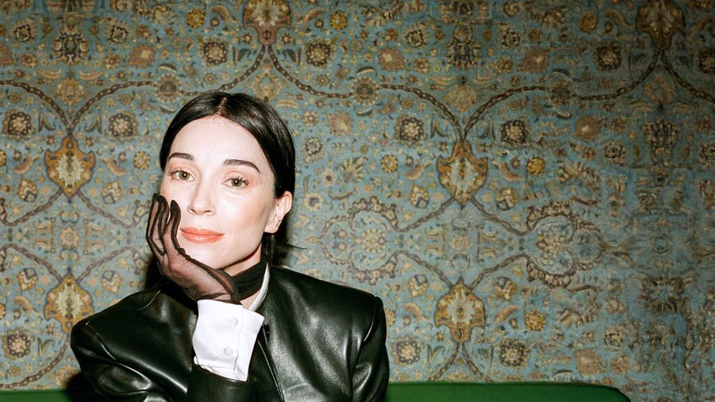 St. Vincent sits with her head in her hand wearing a glove and leather jacket.