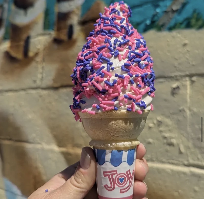 A vanilla ice cream cone with pink and purple sprinkles.