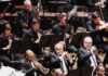 Pittsburgh’s Best Symphonic and Classical Music Concerts in 2026 A section of a symphony with brass players and woodwinds behind them, sitting with music stands.