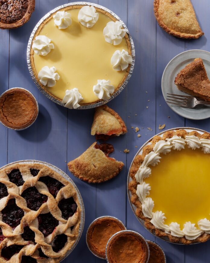 Various pies with whipped cream, lattice tops, and in hand pie shapes sit on a purple picnic table.