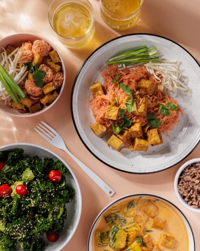 Three bowls of vegan-friendly food like tofu, noodles, salads, and curry.
